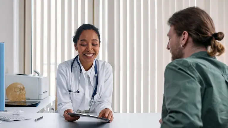 A physician making direct eye contact with a patient in a consultation room while an ambient AI scribe generates a structured SOAP note in the background.